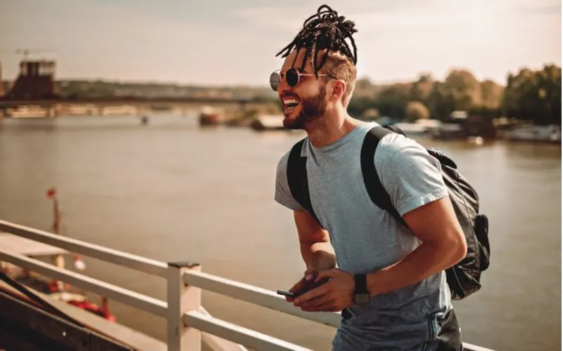 Braided Top Knot Man Bun Haircut worn by a man in a backpack standing in front of a river