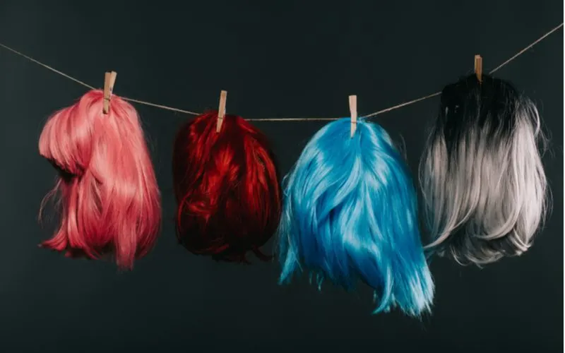Image for a piece on wigs for black women featuring several different colors of wigs hanging from clothespins