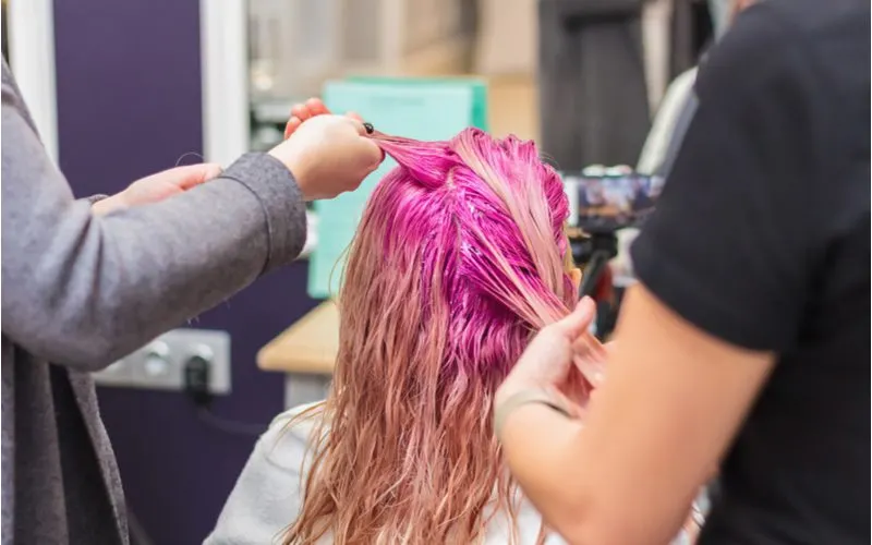 Image for a piece on what removes permanent hair dye from skin featuring a woman in a salon chair getting pink hair
