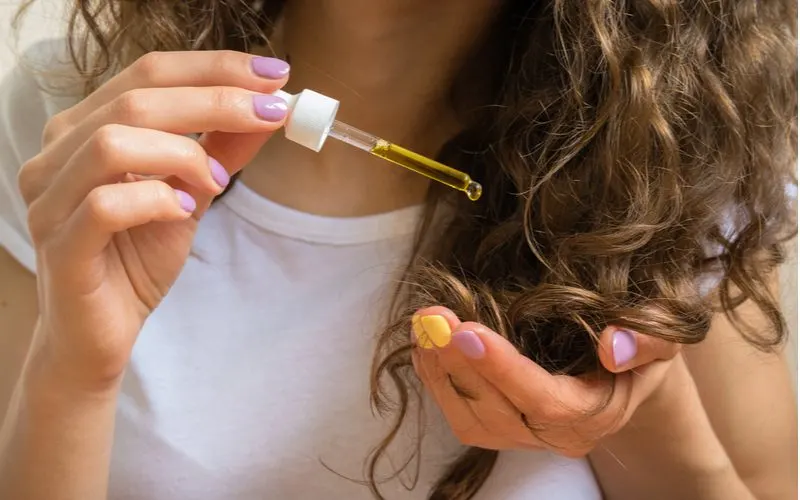 To thicken hair, a woman using a hair serum out of an eyedropper
