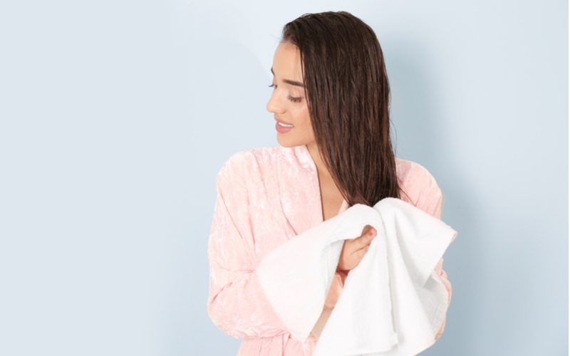 As a step in a guide on how to thicken hair, a woman using a towel to dry her hair