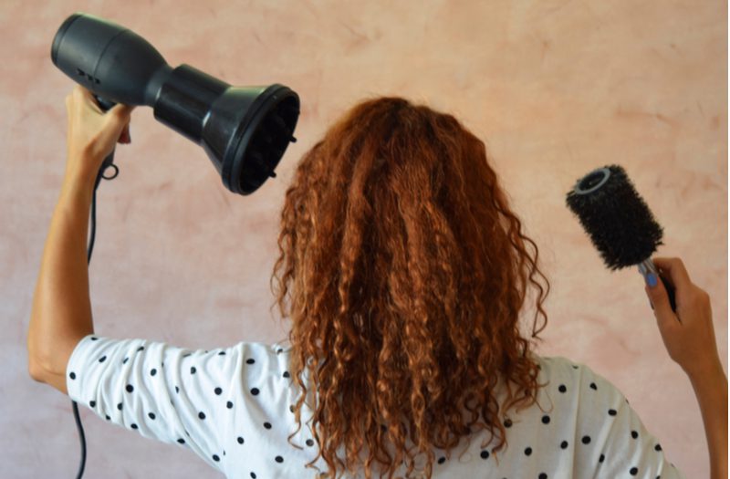 Woman using the best hair dryer for curly hair along with a diffuser