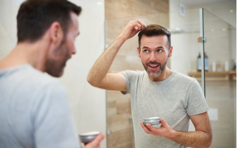 Guy using the best hair gel for thinning hair in the mirror