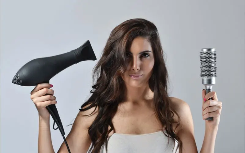 Woman holding a blow dryer and a brush in preparation for getting a 90s blowout