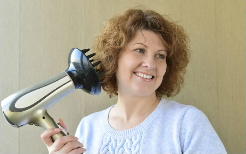 Normal looking woman taking steps to fix her damaged hair by using a diffuser