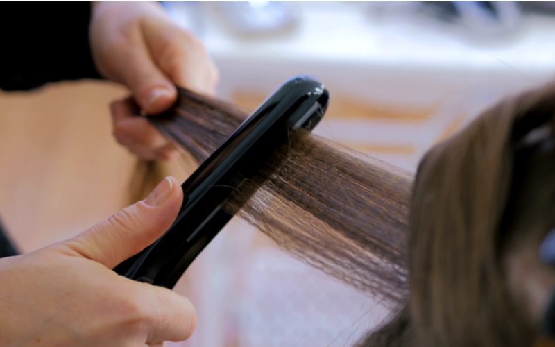 Woman styling curtain bangs with a flat iron