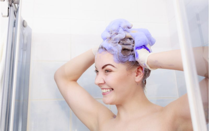 Woman using purple shampoo on brown hair in a shower