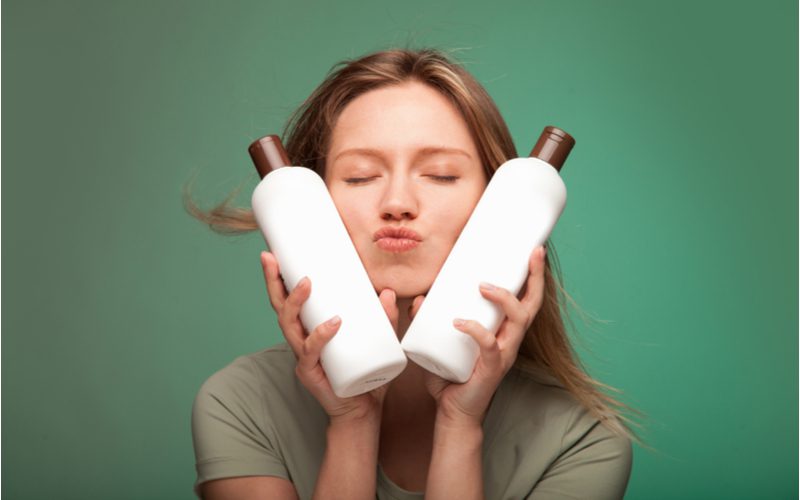 Woman holding up two bottles of the best curl cream for wavy hair in a green room