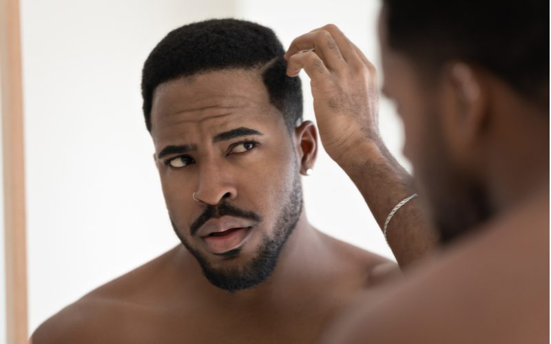 Image of a black guy looking in the mirror for a piece titled best moisturizer for black men's hair