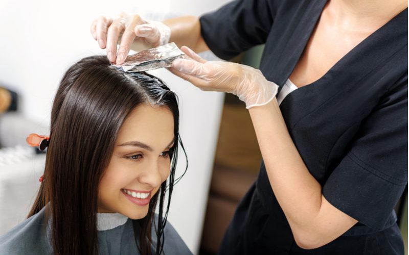 For a piece on what is Demi-Permanent Hair Color, a woman smiling as she gets her hair dyed by a stylist
