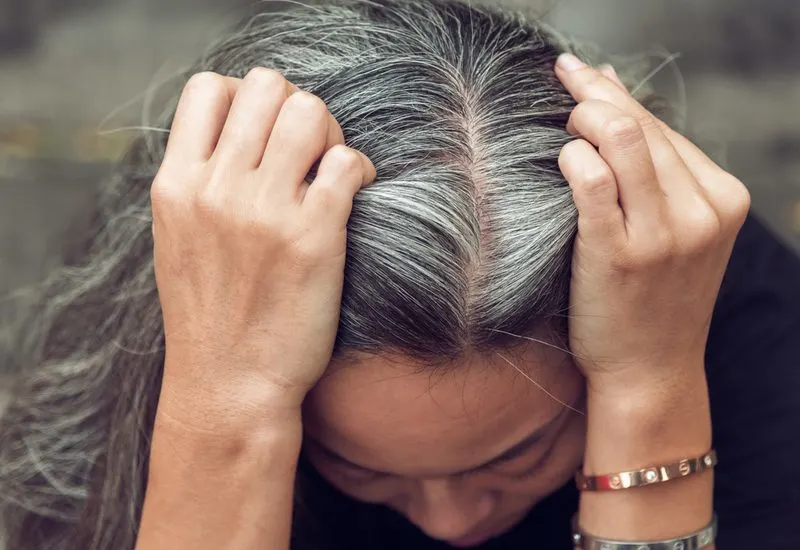Woman holding her head after showing us how to use color-depositing conditioner on her gray hair