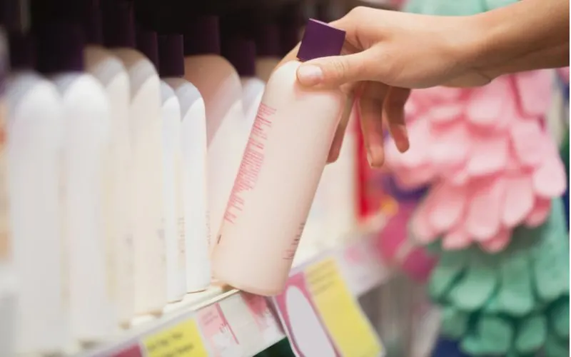 Woman's hand grabbing a bottle of hair product off a shelf and showing us how to use color-depositing conditioner
