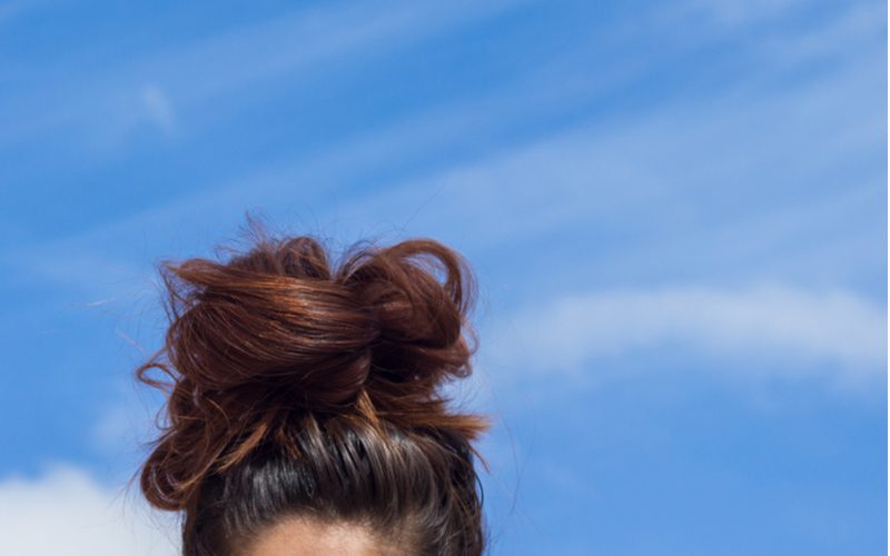 Photo of someone showing us how to make a cute messy bun in a close-up image against the sky