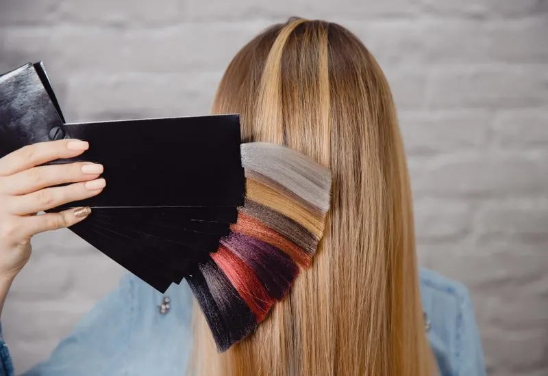 For a piece titled what color should I dye my hair, a stylist holding a few hair samples up to the client's hair