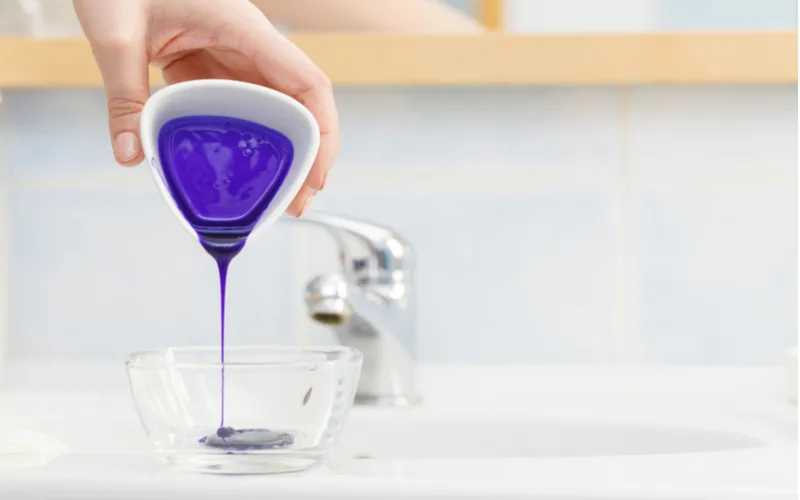 Woman pouring purple hair toner into a glass dish for a piece titled should I tone my hair before dying it