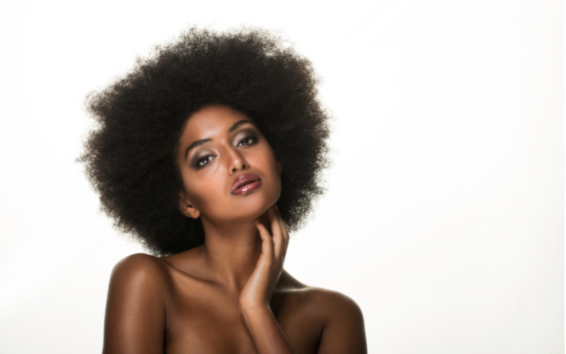 Woman with the 4C hair type in a studio holding her neck
