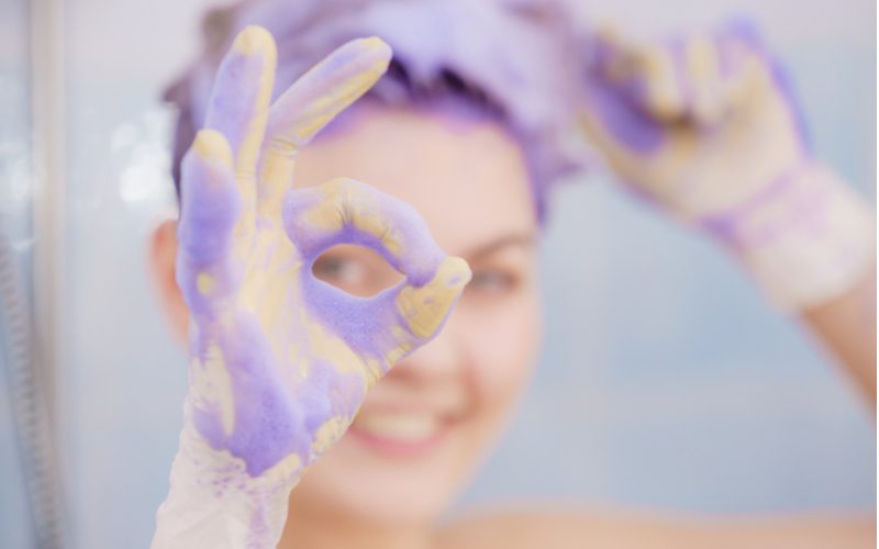 Woman removing purple shampoo stain from hair and giving an ok sign with her fingers