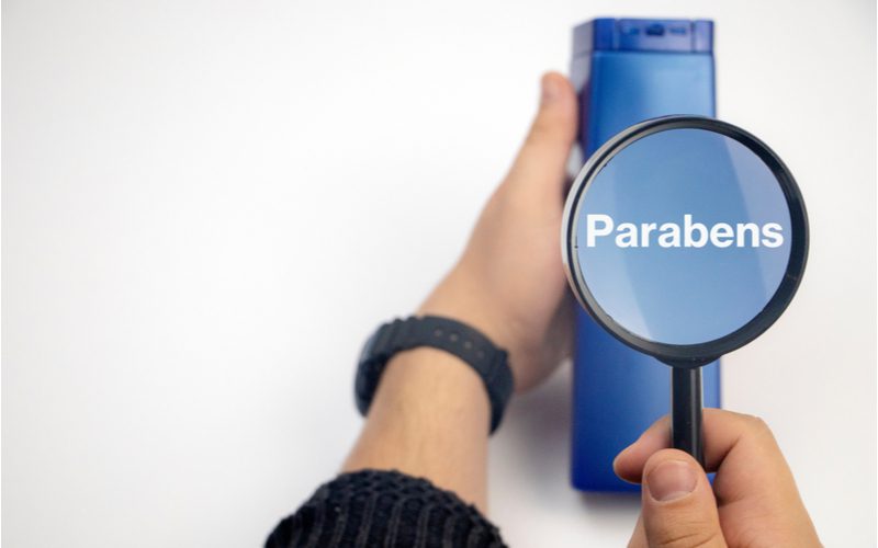 Image for a piece on what are the main ingredients in shampoo featuring a magnifying glass held up to a bottle that says parabens