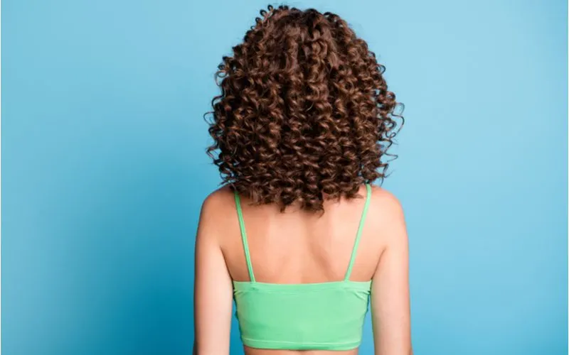 Image for a piece on how to get tight curls featuring a woman in a blue room facing a wall with tight curls