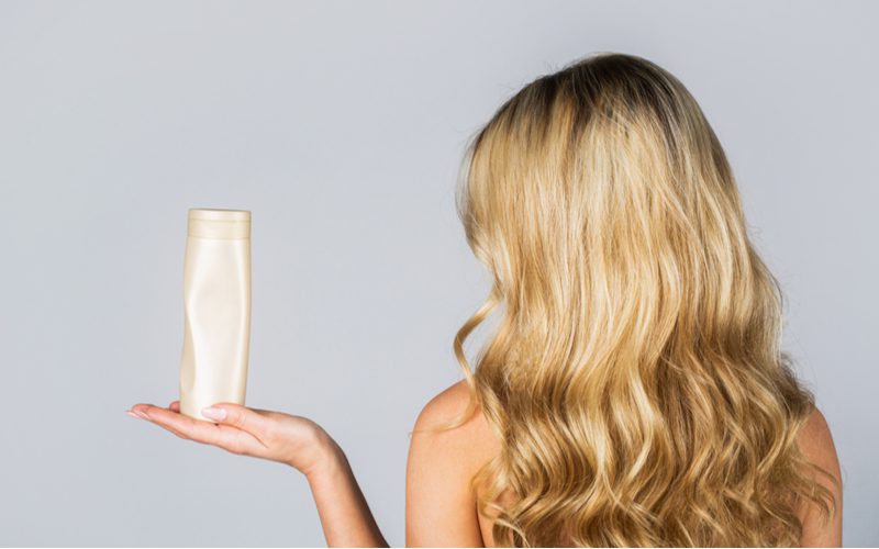 Woman holding a bottle of clarifying shampoo to fix over-toned hair
