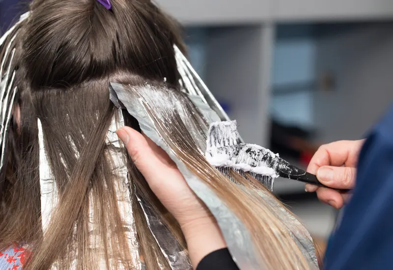 Woman getting hair highlights for a piece titled highlights vs single process hair color