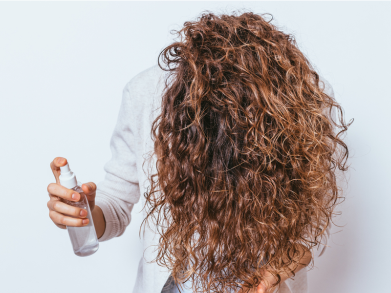 Người phụ nữ sử dụng bình xịt gỡ rối trên mái tóc đã được chải kỹ của mình để xem một đoạn về cách gỡ rối tóc đã chải