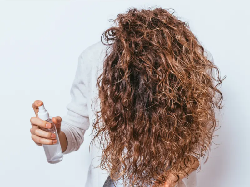 Woman using a detangling spray on her matted hair for a piece on how to detangle matted hair