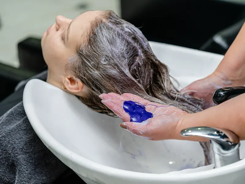 Woman fixing a bad peroxide hair dye job with purple shampoo in the salon
