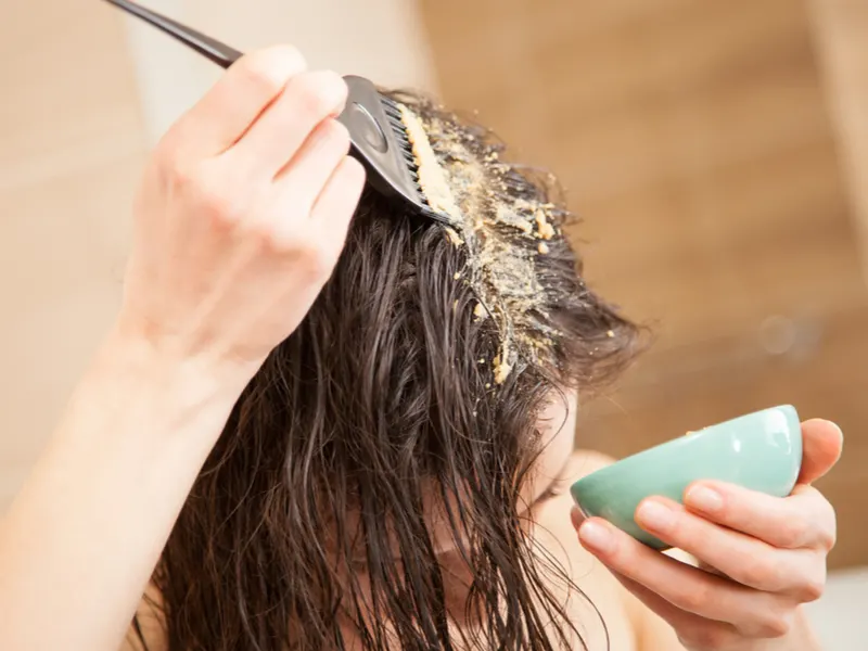 Woman applying a bentonite clay hair mask to her head