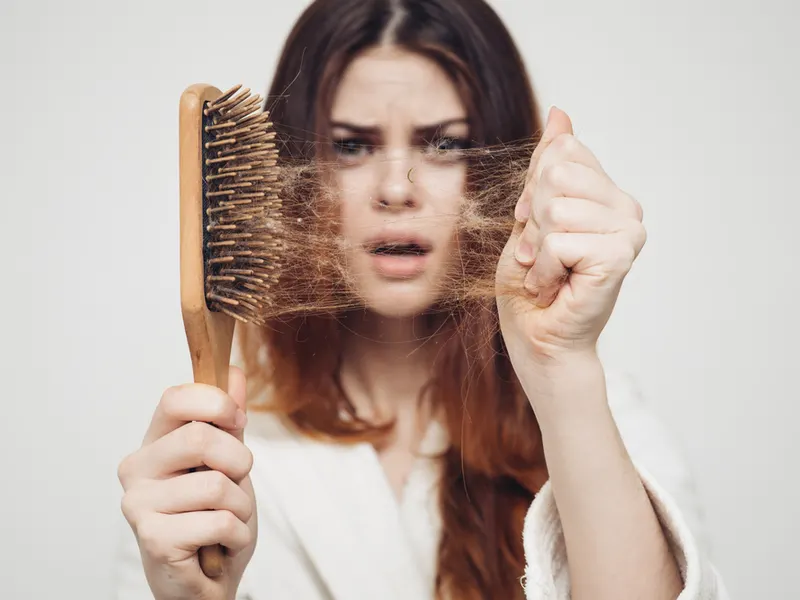 Woman wondering, "why is my hair falling out" while holding a brush with hair in it