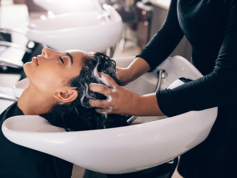 Woman wondering how much to tip the shampoo girl with her head in the shampoo bowl