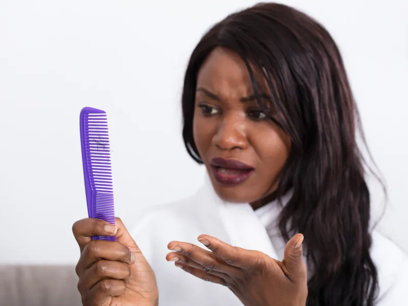 Black woman who needs the best hair moisturizer for relaxed hair looking at her hair breakage on the comb
