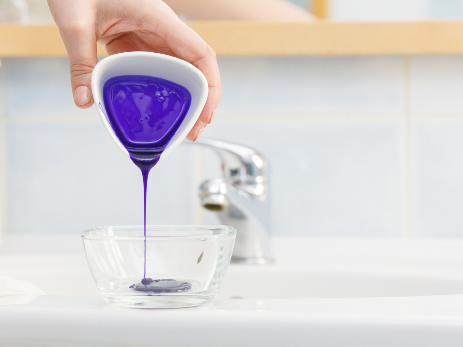 Woman pouring purple shampoo into a glass bowl for a piece titled do you apply toner to wet or dry hair