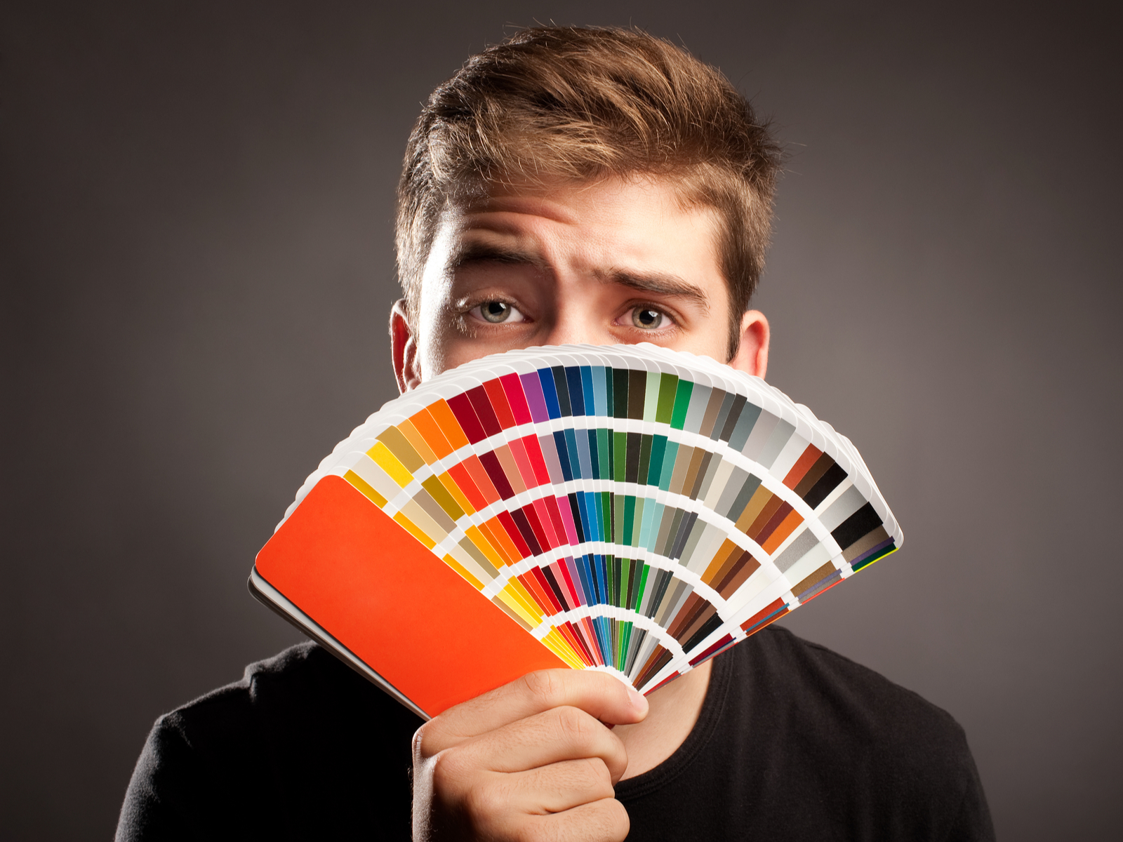 Guy holding a color palate sample in front of his face for a piece on the best hair color ideas for men