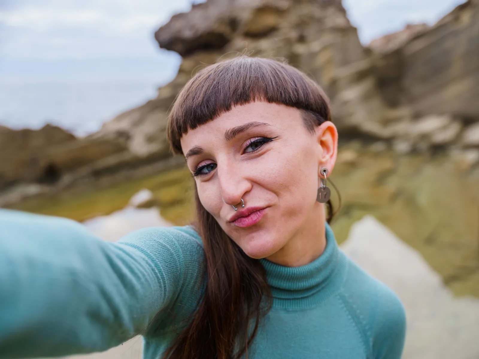 Woman with a Disconnected Mushroom Cut Mullet Type taking a selfie on a hike in a rocky area
