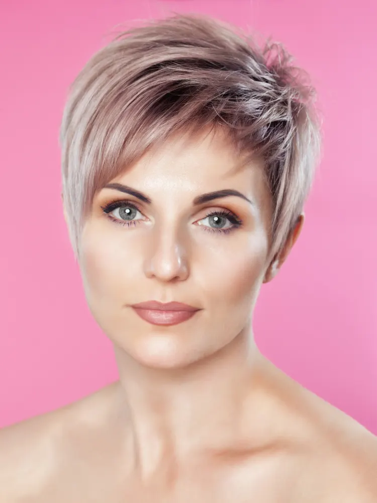 Woman with a short grey hairstyle for women in a pink room with a pixie cut combed to the left