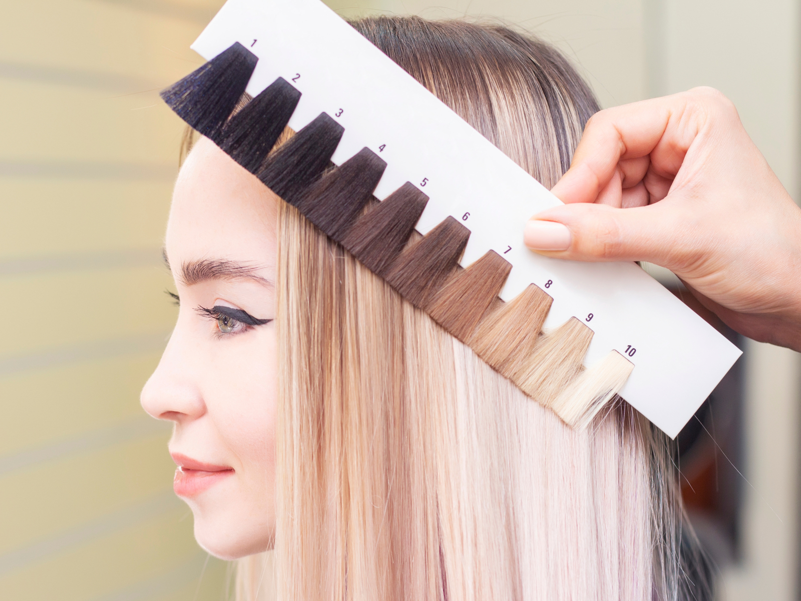 Woman using the color wheel hair theory to find shades of color that work on her by holding up swatches of dyed hair to her head