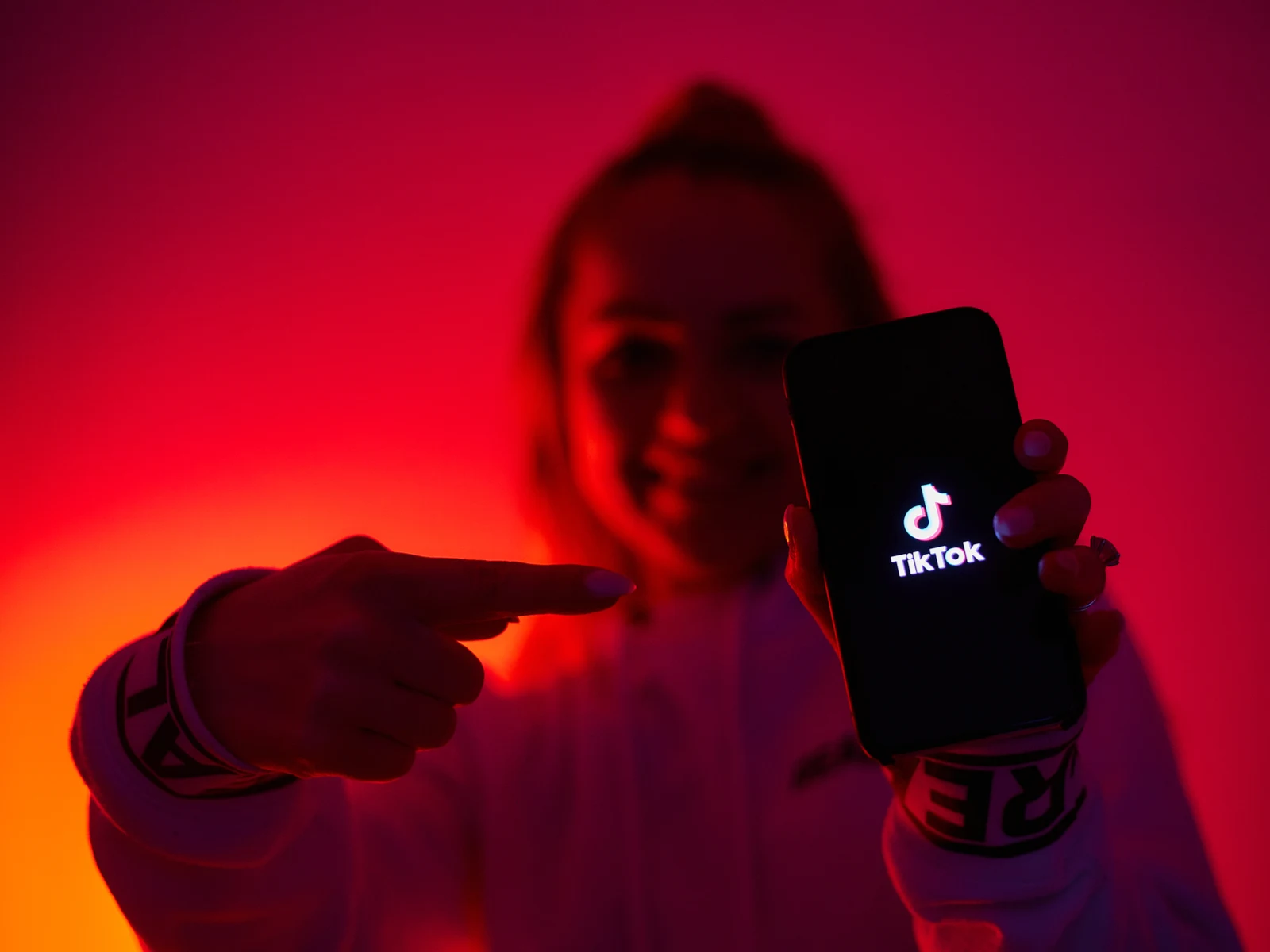 Young woman pointing to a phone with the TikTok app for a piece on TikTok hair trends