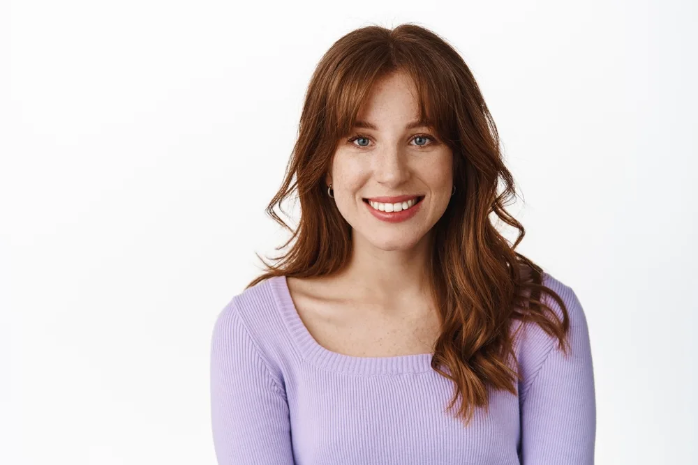 Short and Chic French Bangs on a woman in a purple sweater with red hair