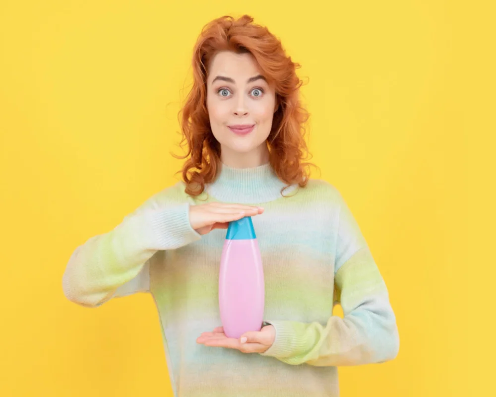 Ginger woman holding the best shampoo for red hair with a sweater and standing in a yellow room