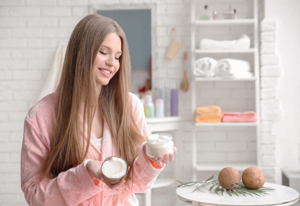 Woman using coconut oil before bleaching hair while holding a coconut and a jar of the stuff