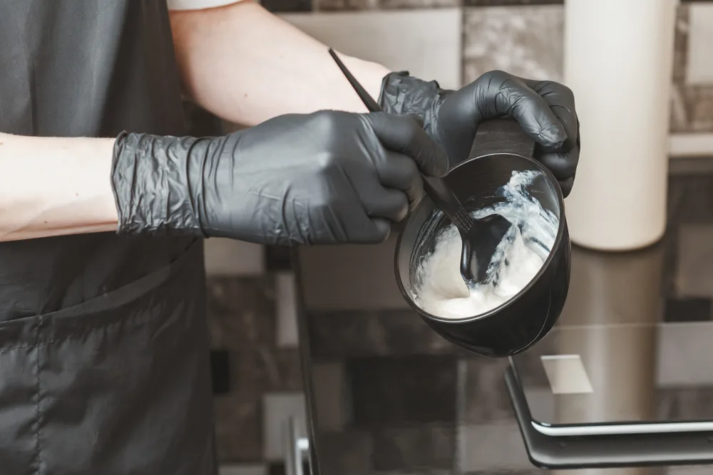 Gloved hairdresser mixing a bowl of color for a piece on does hair bleach expire
