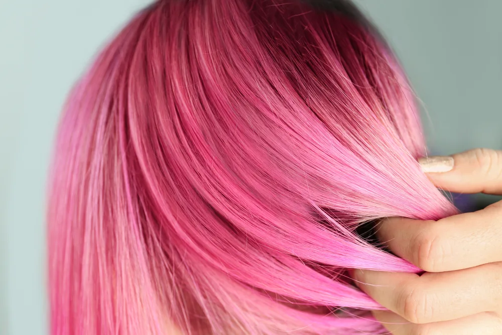 For a piece on the best unnatural hair colors for blue eyes, a woman wearing Light Raspberry Pink hair runs her hand through her hair