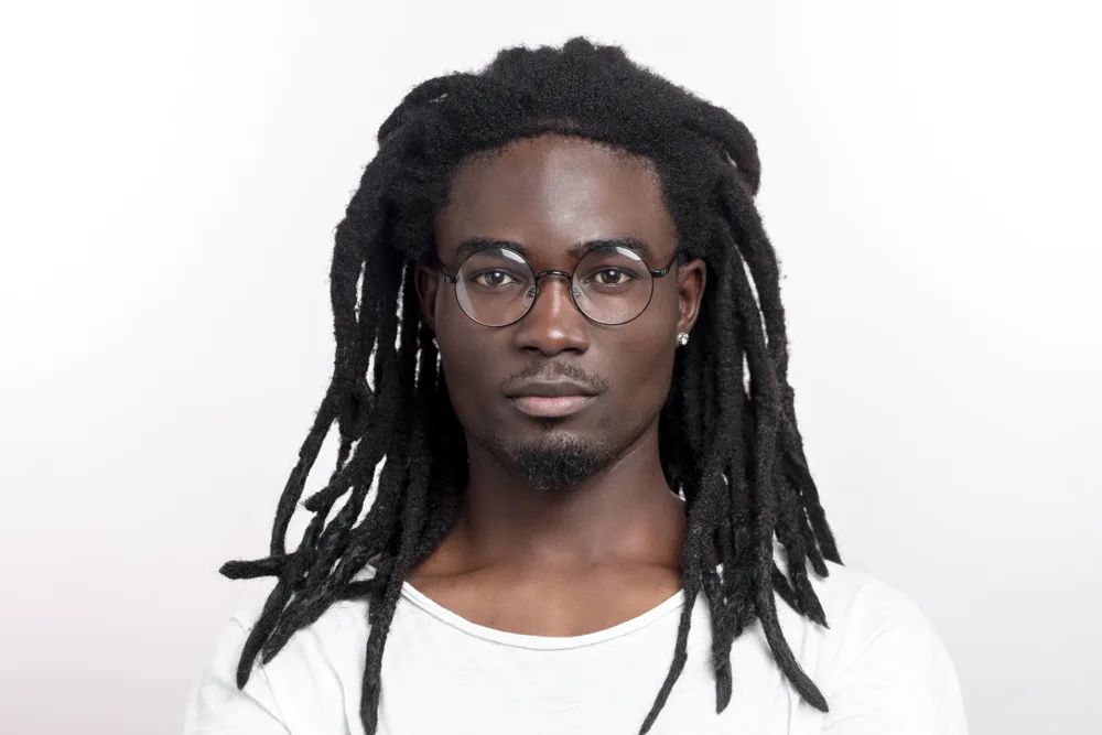 Wick Dreads hairstyle on a guy in glasses in a white room