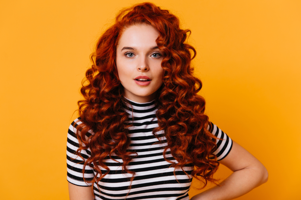 Darkened Copper ginger hair color idea on a woman wearing a black and white striped shirt in an orange room