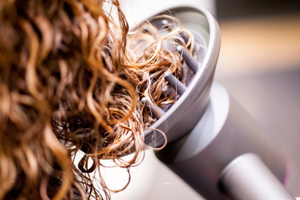 Hình ảnh một người phụ nữ sử dụng máy khuếch tán trên mái tóc mỏng được uốn của mình