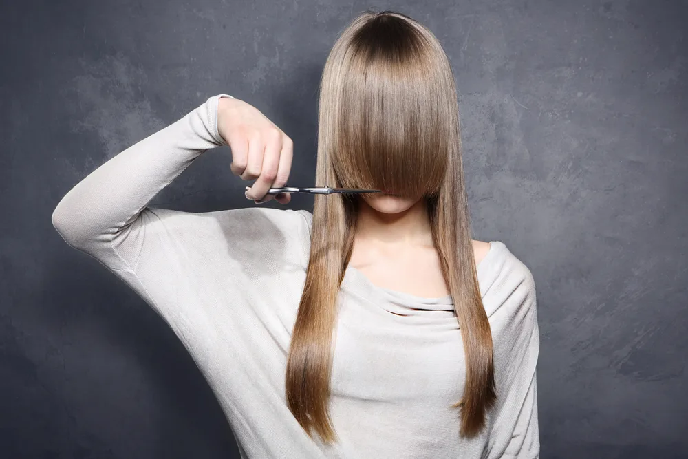 Woman clipping her hair to make bangs in a taupe sweater
