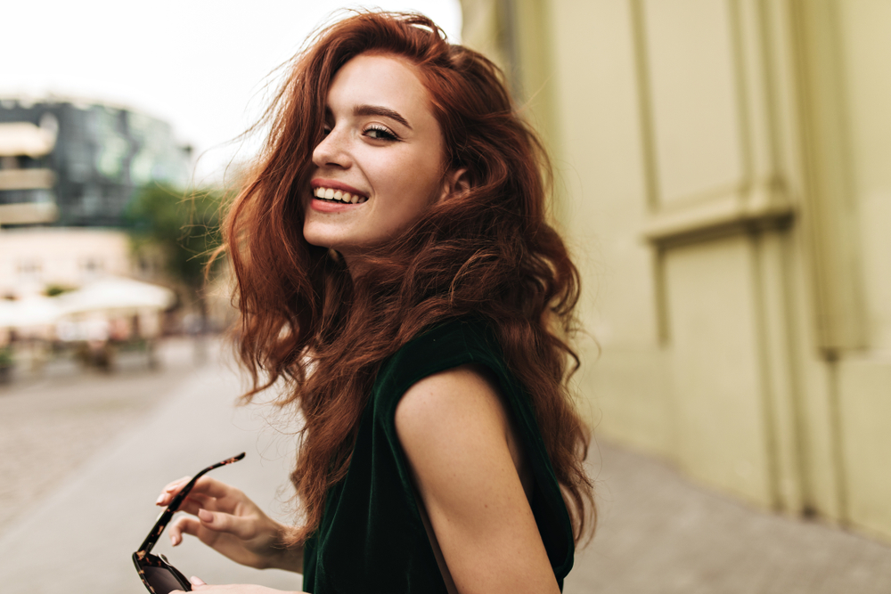 To help illustrate the best hair colors for neutral skin tones, a woman smiling outside