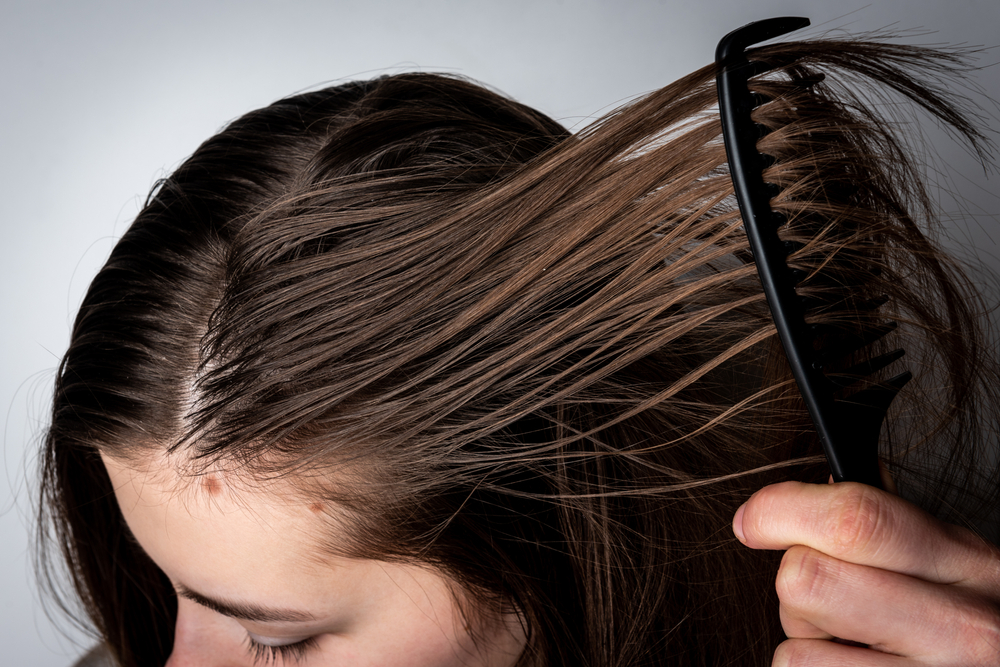Woman with oily hair runs a comb through her hair