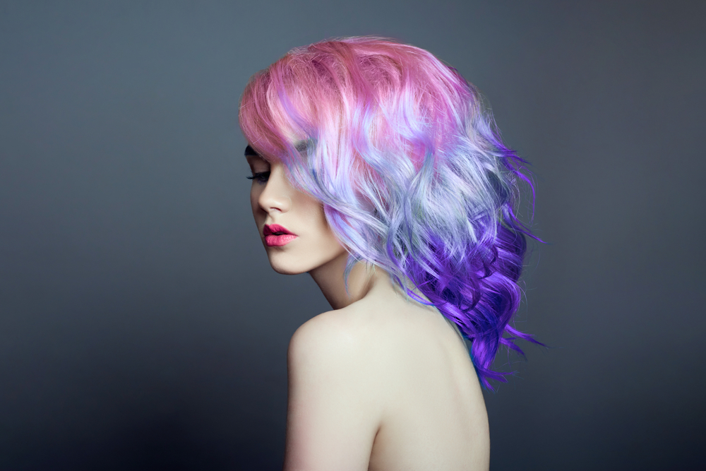 Bubblegum Pink to Violet Ombre, one of the best unnatural hair colors for blue eyes, on a woman in a grey room